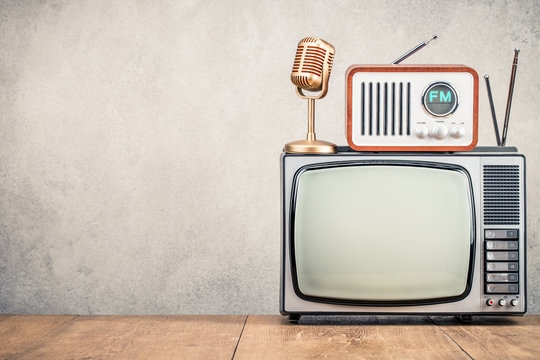 Vintage radio and microphone on top of an old television set against a plain wall.